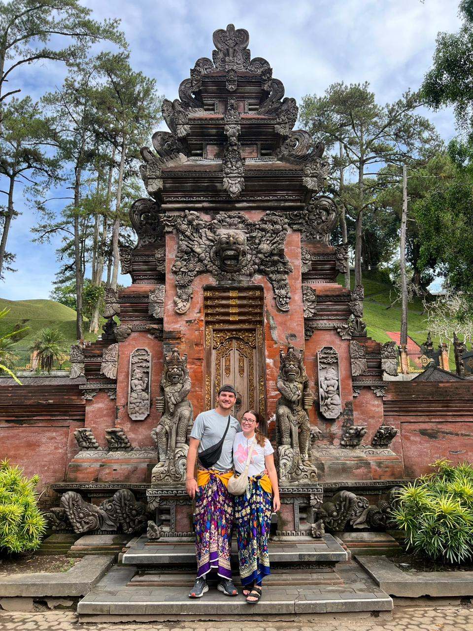 Couple in sarongs in front of a red brick Balinese temple
