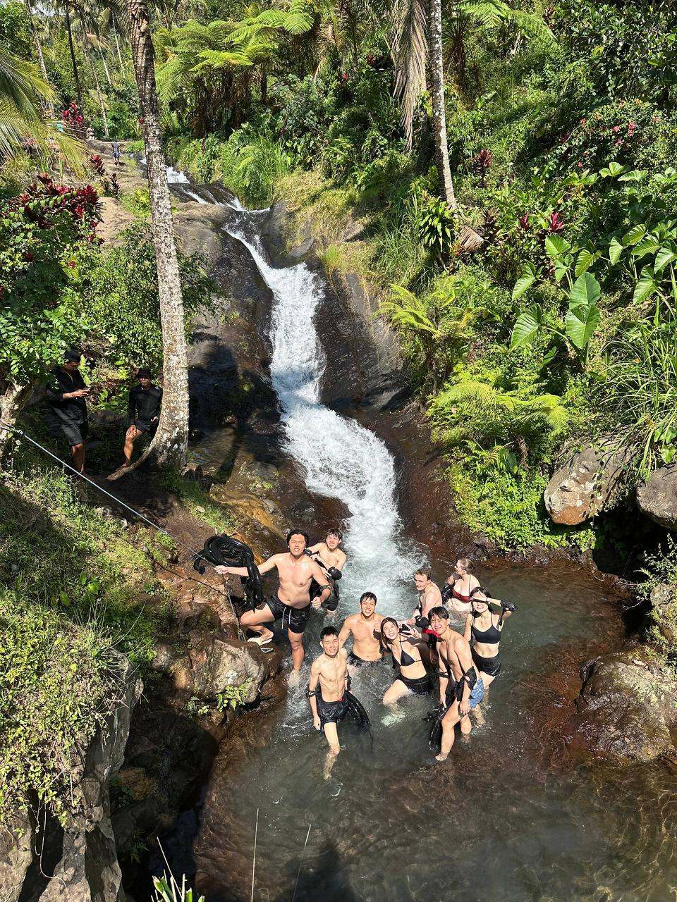 Group swimming in a natural pool below a waterfall
