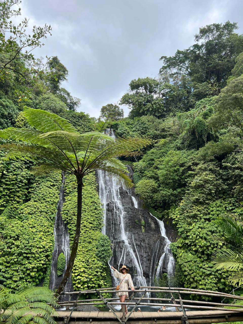 Guest on a bridge below a waterfall covered in ferns