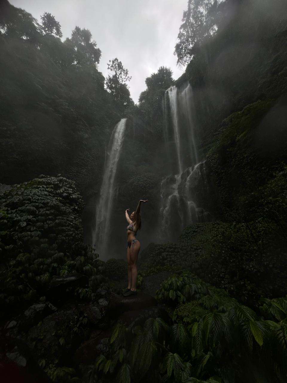 Guest standing at the base of a tall waterfall in the mist