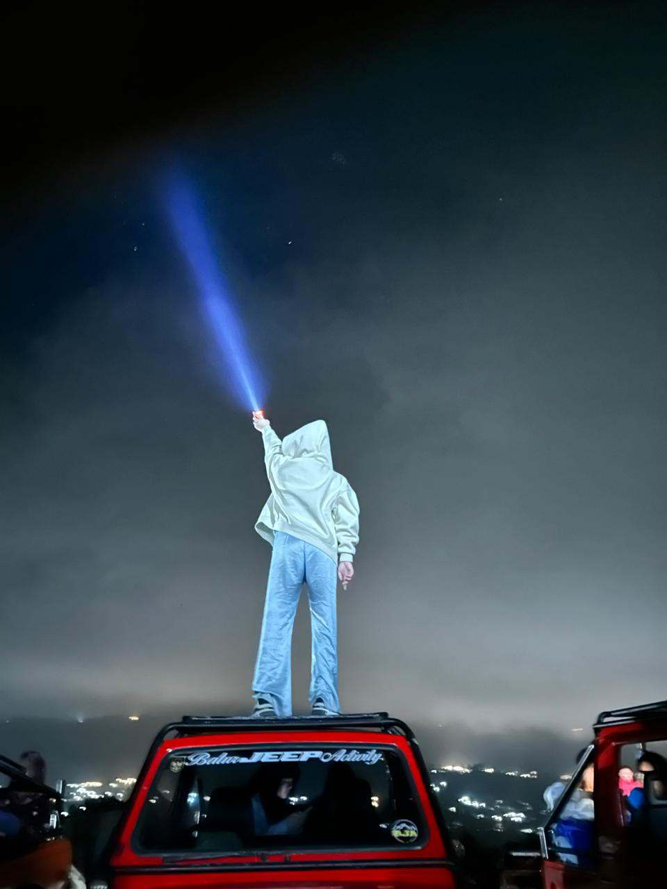 Guest standing on a jeep pointing a light beam at the stars