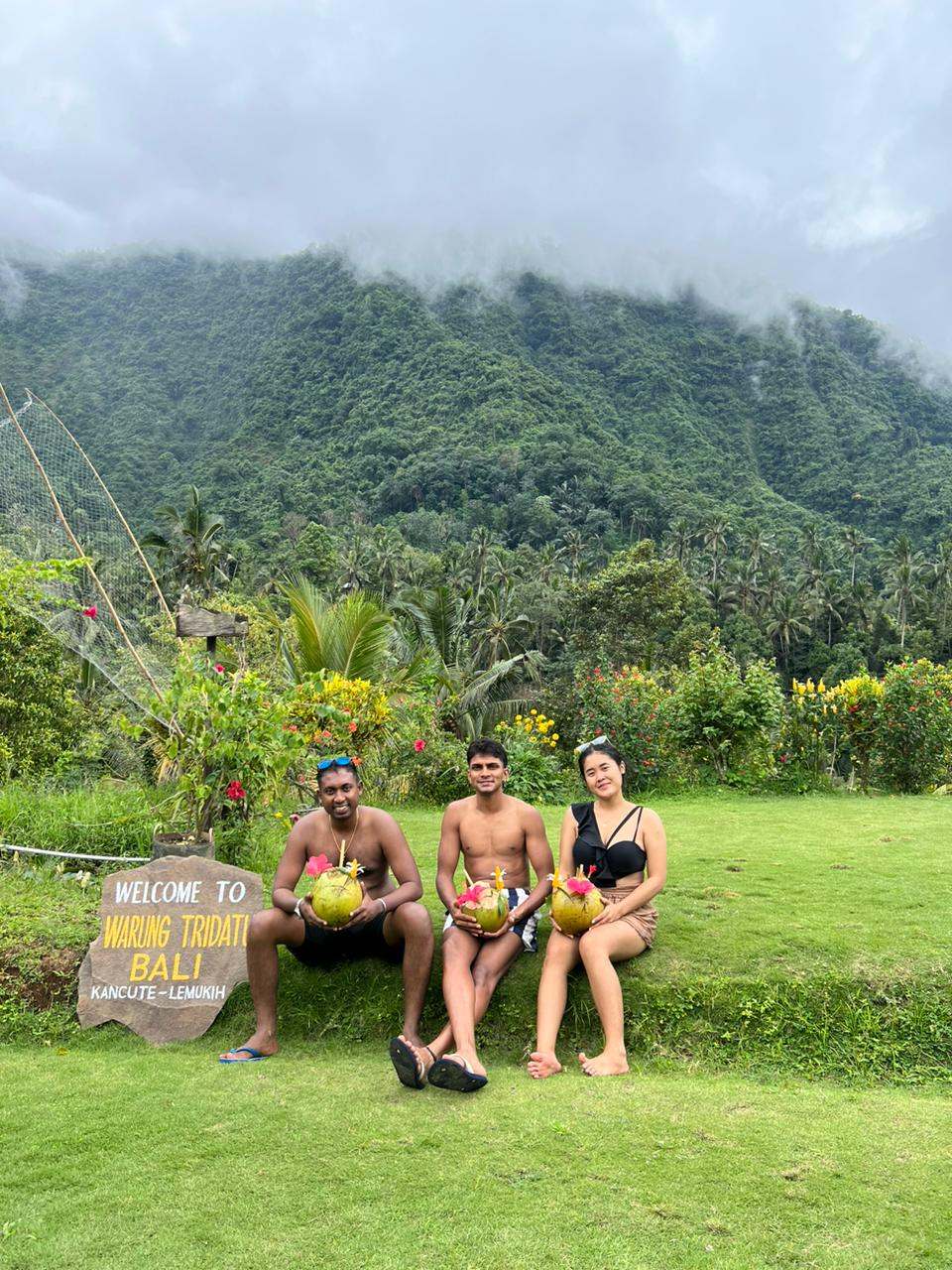 Guests with coconuts on a lawn below green hills