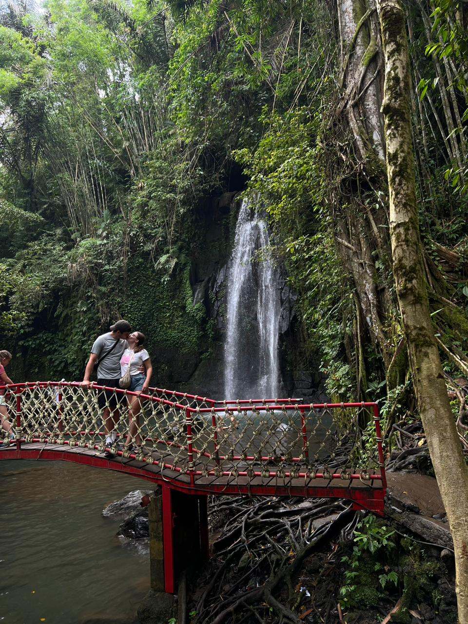 Guests on a red bridge looking at a jungle waterfall