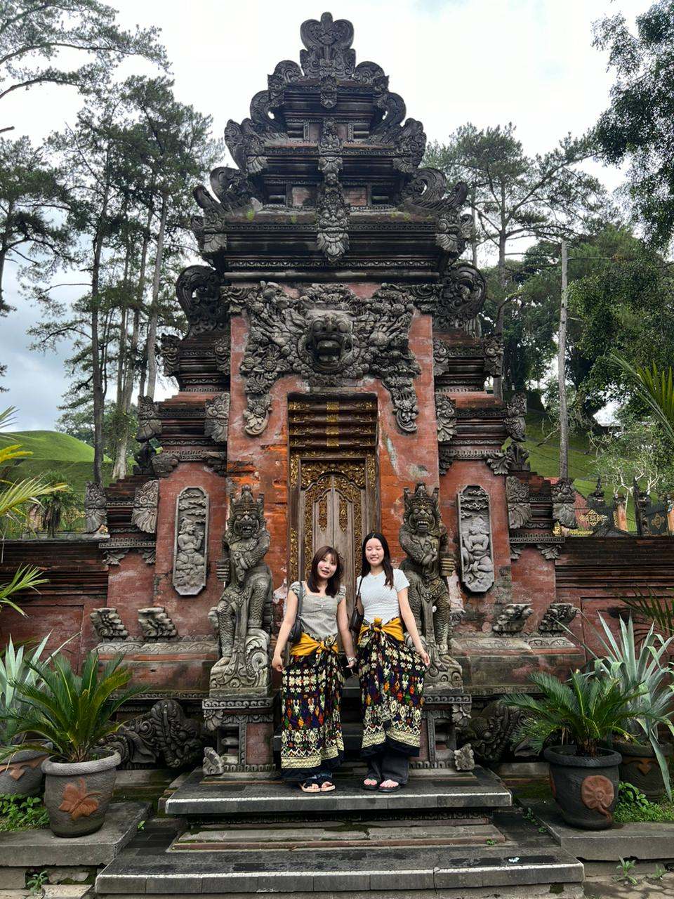 Two guests in sarongs in front of a carved Balinese temple gate