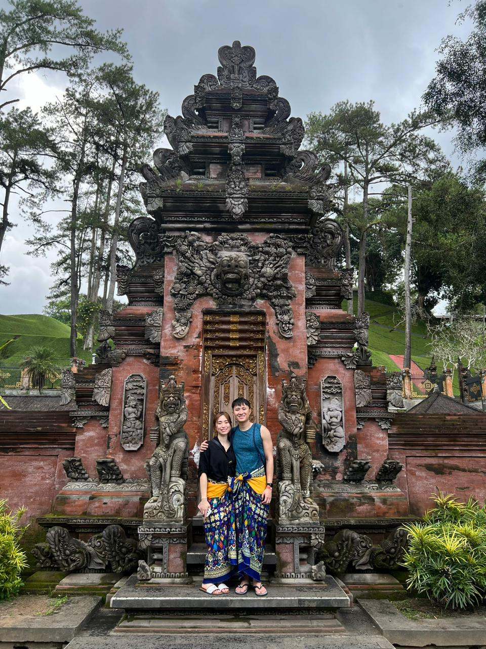 Two guests in sarongs in front of a red brick Balinese temple