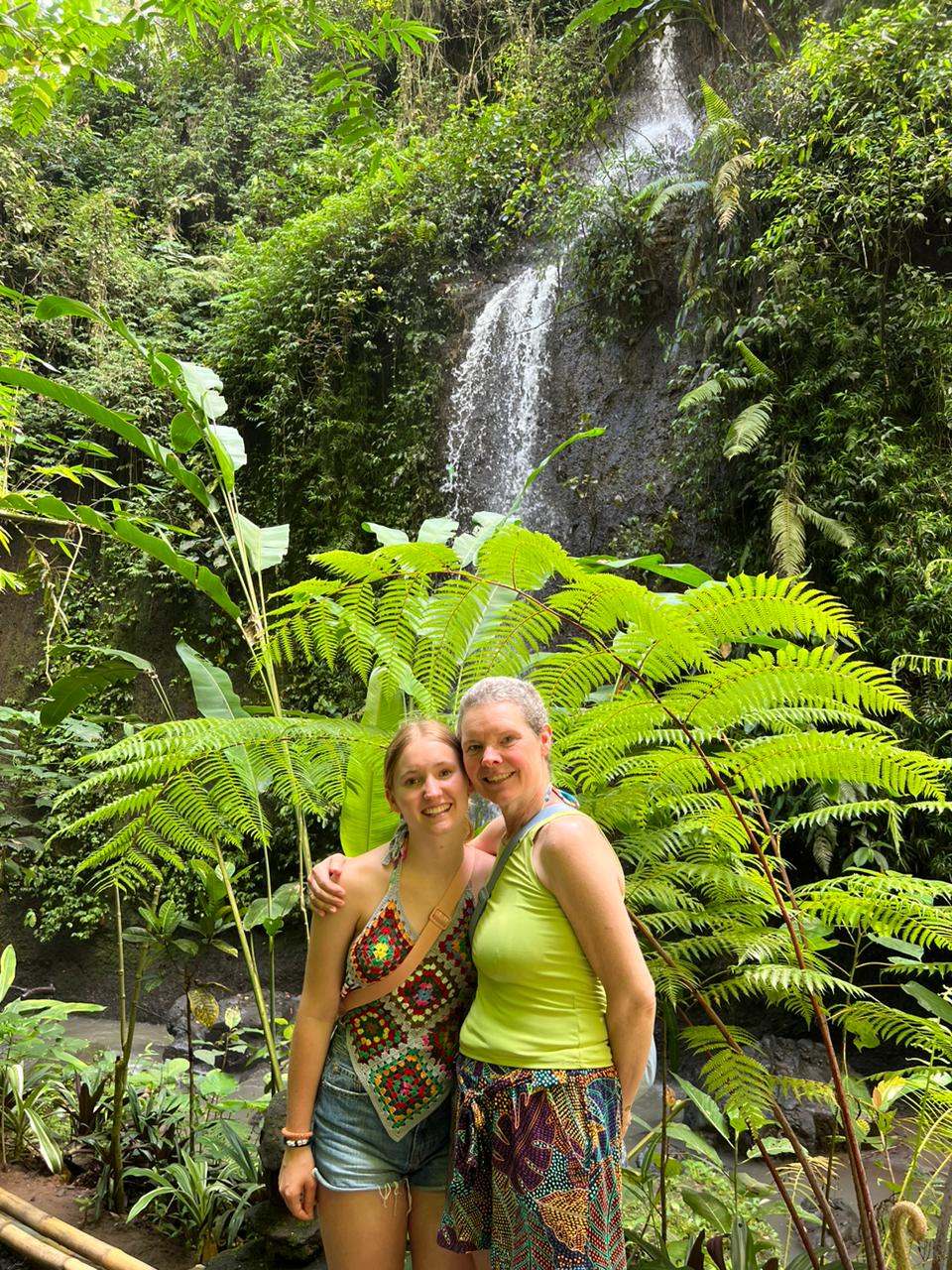 Two guests smiling in front of a jungle waterfall