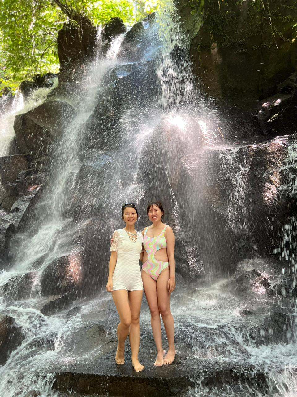 Two guests in swimsuits under a waterfall